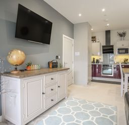 A living room with a mounted TV a cabinet and a kitchen area at The Pot Loft in Benllech