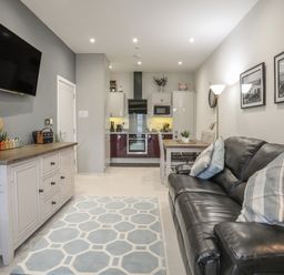 A living room with a black leather sofa and blue patterned rug next to a dining table and open kitchen at The Pot Loft in Benllech