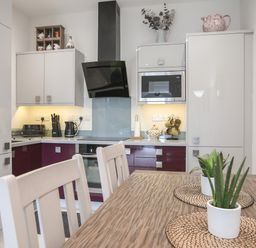 A kitchen with white and maroon cabinets a wooden table with plants on placemats and kitchen appliances at The Pot Loft in Benllech