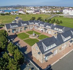 A stone house building arranged in a u shape with a central courtyard garden and fountain in a rural area at Tyn Towyn - Bwthyn Carreg in Trearddur Bay