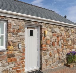 Exterior stone wall of a building with a white door and two white windows at Tyn Towyn - Bwthyn Carreg in Trearddur Bay