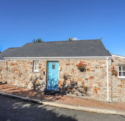 A stone cottage with a blue door and windows with hanging flower baskets at Tyn Towyn - Bwthyn Haf in Trearddur Bay