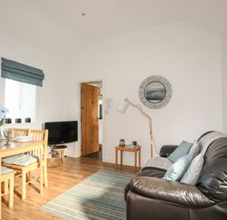 A living room with a brown leather sofa, dining table with chairs, and a television at Tyn Towyn - Bwthyn Haf in Trearddur Bay