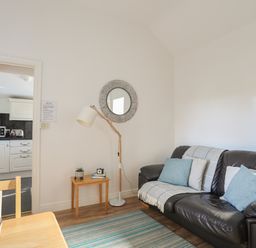 A living room with a black leather sofa cushions and a lamp next to a wooden table at Tyn Towyn - Bwthyn Haf in Trearddur Bay