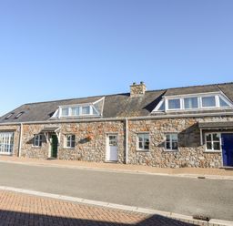 A stone building with three doors and multiple windows along a street at Tyn Towyn - Ty Glas in Trearddur Bay