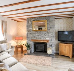 A living room with a stone fireplace wooden beams a sofa and a television at Tyn Towyn - Ty Oren in Trearddur Bay