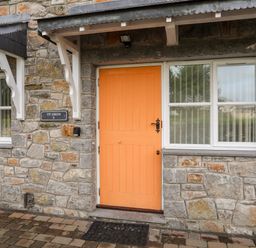 A stone exterior wall with an orange door and windows at Tyn Towyn - Ty Oren in Trearddur Bay