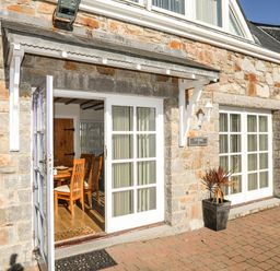 Stone building exterior with white framed glass doors and wooden chairs visible inside at Tyn Towyn - Ty Piws in Trearddur Bay