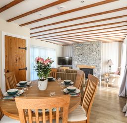 A dining area with a wooden table and chairs and a stone fireplace in a living room at Tyn Towyn - Ty Piws in Trearddur Bay