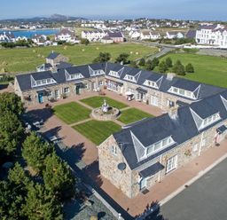 A stone building arranged in a U shape around a central lawn with a fountain and pathways at Tyn Towyn - Ty Piws in Trearddur Bay