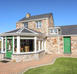A stone house with green doors and large windows and a paved walkway with grass at Tyn Towyn - The Stables in Trearddur Bay