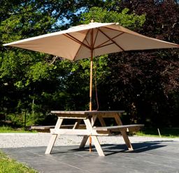 A wooden picnic table with a large beige umbrella on a patio surrounded by trees at Tyddyn Morthwyl in Criccieth