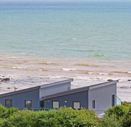 A coastal scene with modern houses near the shore and ocean waves behind at Ty Glyn in Criccieth