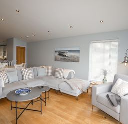 A living room with a gray sectional sofa and armchair a coffee table and a painting on the wall at Ty Glyn in Criccieth
