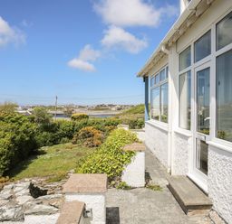 Exterior view of a building with white walls and windows overlooking a garden and distant buildings at Ty Llwyd in Trearddur Bay