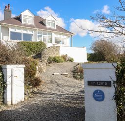 A house with a gravel driveway and white pillars at the entrance at Ty Llwyd in Trearddur Bay