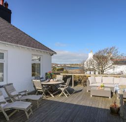 An outdoor deck with wooden chairs a round table a cushioned sofa and a small coffee table at Ty Llwyd in Trearddur Bay