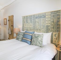 A bedroom with a bed with patterned cushions and a tapestry headboard two bedside tables with lamps a wooden door and a chest of drawers with a mirror at Ty Mawr Porthmadog in Porthmadog