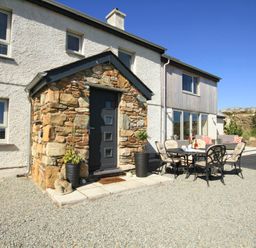 A house exterior with a stone porch and outdoor dining table with chairs on gravel at Ty Nant in South Stack