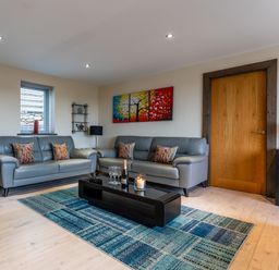 A living room with two gray sofas a colorful painting a blue patterned rug and a black coffee table at Ty Nant in South Stack