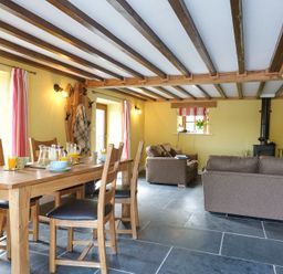A dining area with a wooden table set for breakfast and a living area with sofas and a wood stove at Tyn Llwyn Cornel in Beddgelert