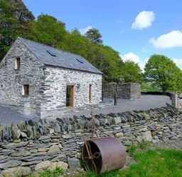 A stone house with a slate roof next to a stone wall and a metal roller by a wooden gate in a rural area at Tyn Llwyn Cornel in Beddgelert