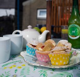 A table with cupcakes in colorful wrappers a teapot two white mugs and a green bottle at 17 Victoria Terrace - Perthi in Nantlle