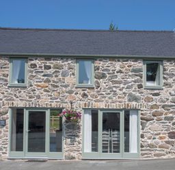 Stone exterior of a cottage with four windows two glass doors and a hanging basket of flowers at Mulberry Cottage in Pentraeth