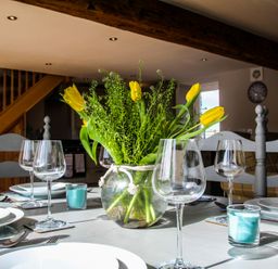 A dining table set with plates glasses and a vase of yellow flowers in a room with wooden stairs at Mulberry Cottage in Pentraeth