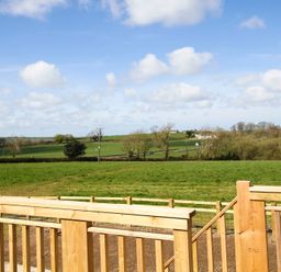 A view of green fields with scattered trees and a wooden fence in the foreground at Mulberry Cottage in Pentraeth