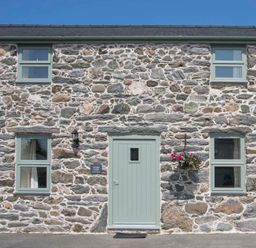 Exterior view of a stone cottage with four windows and a centered front door with flower pot at Partridge Cottage in Menai Bridge