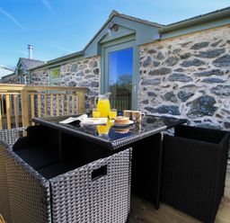 A patio with a black wicker table and chairs a jug of orange juice two glasses a cake and two mugs at Partridge Cottage in Menai Bridge
