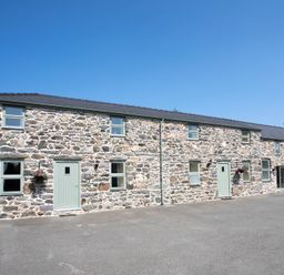 A stone building with multiple windows and light green doors under a clear blue sky at Partridge Cottage in Menai Bridge