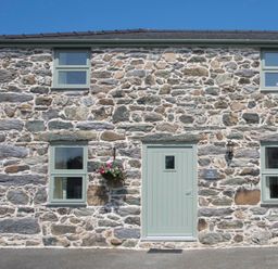 Stone cottage with green door and windows and a hanging flower basket at Teal Cottage in Menai Bridge