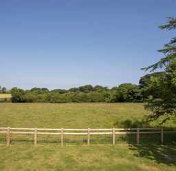 A grassy field with a wooden fence and trees under a clear sky at Teal Cottage in Menai Bridge