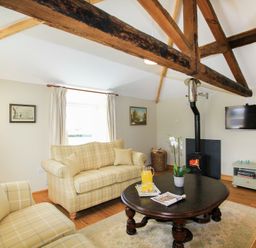 A living room with exposed wooden beams sofas a coffee table a wood stove and a wall mounted TV at Teal Cottage in Menai Bridge