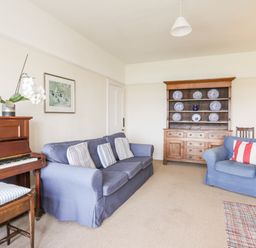 A living room with a blue sofa and armchair a wooden piano and cabinet with decorative plates at Windygates in Rhosneigr