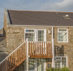 A stone building with external wooden stairs and white framed windows at Potters by the Sea in Sennen