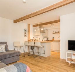 A living room with a gray sofa and kitchen with bar stools at Potters by the Sea in Sennen