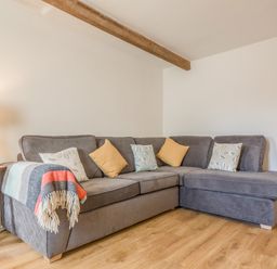 A corner grey sofa with pillows and a blanket next to a lamp on a wooden floor at Potters by the Sea in Sennen