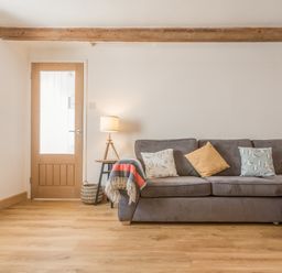 A living room with a gray sofa and cushions a wooden door and a floor lamp at Potters by the Sea in Sennen