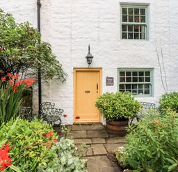 Front view of a white cottage with a yellow door green windows plants and metal chairs at Bonny Bits Cottage Garrigill near Alston