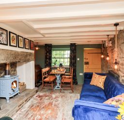 A living room with a blue sofa a wood stove a wooden dining table with chairs and hanging pendant lights at Bonny Bits Cottage in Garrigill near Alston