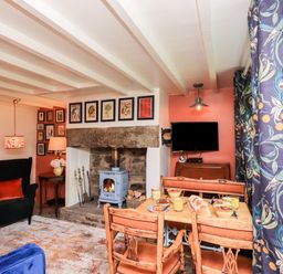 A living room with a wood stove fireplace dining table with food and chairs a patterned curtain and a television at Bonny Bits Cottage in Garrigill near Alston