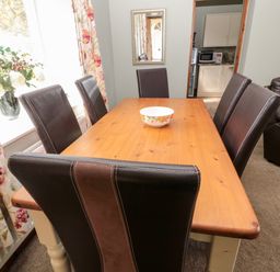 A dining area with a wooden table and six brown chairs a bowl on the table floral curtains and a flower vase on the windowsill Forge Cottage Rothbury