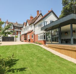 A garden with a grass lawn and a modern glass extension attached to a traditional house at The Coach House in Teignmouth