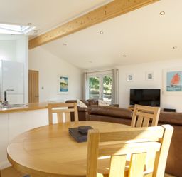 A kitchen and living room with a wooden dining table and chairs leather sofas a TV and framed pictures at 3 Valley View in Lanreath