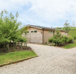 A wooden single-story building with small trees and gravel driveway at 3 Valley View in Lanreath