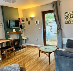 A living room with a wooden dining table and chairs a sofa and coffee table a fireplace with a mounted TV and a door leading outside at Wellinghill Lodge in Cheltenham