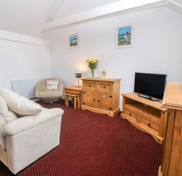 A living room with a beige sofa a round chair wooden cabinets a television and wall art at The Stables in Longrock